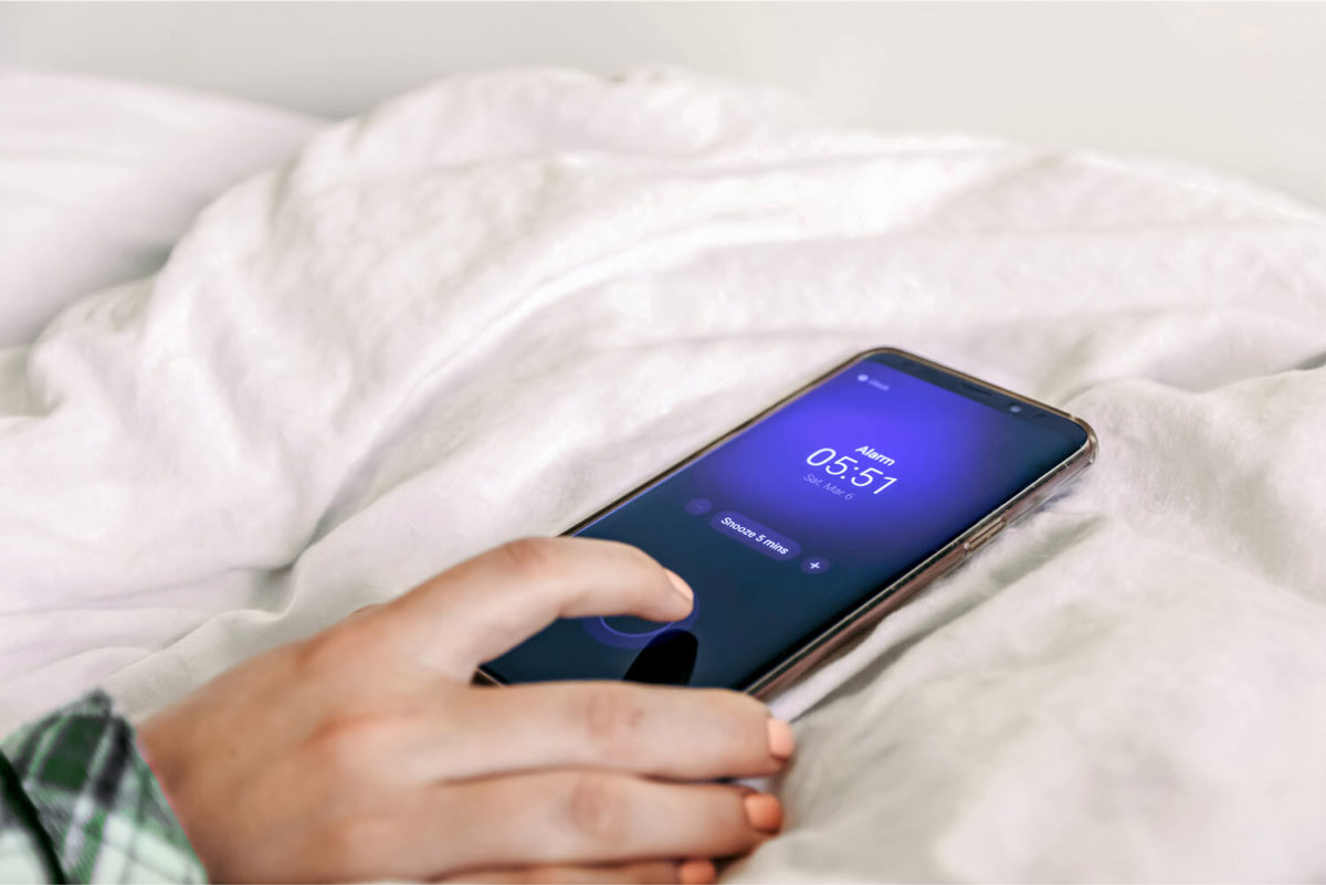 Close-up image of hand snoozing alarm clock on mobile phone.